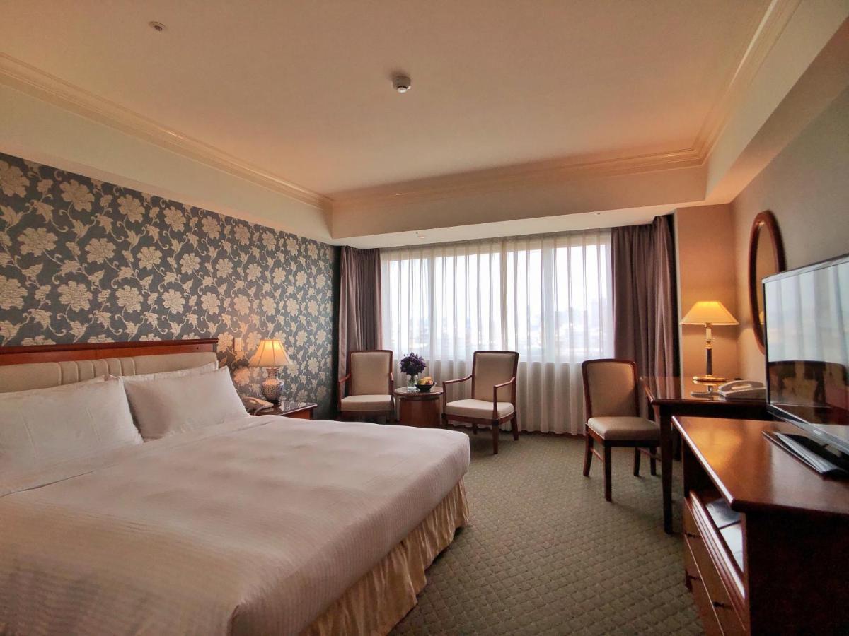 Evergreen Laurel Hotel - Тайчжун Экстерьер фото The photo shows a well-appointed hotel room. It features a large bed with white bedding and a decorative headboard. The walls are adorned with a patterned wallpaper, possibly floral, adding a touch of elegance. There is a window with sheer curtains t