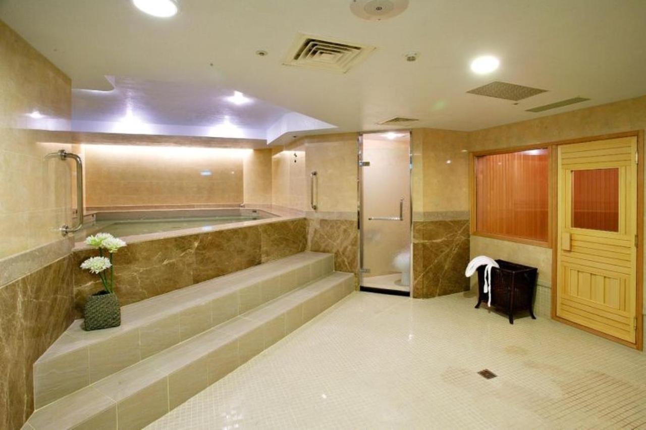 Evergreen Laurel Hotel - Тайчжун Экстерьер фото The photo shows a spacious and well-lit spa or wellness area. It features a large, recessed hot tub with steps leading up to it, surrounded by beige marble walls. There's a shower area enclosed in glass, and to the right, a wooden sauna or steam room