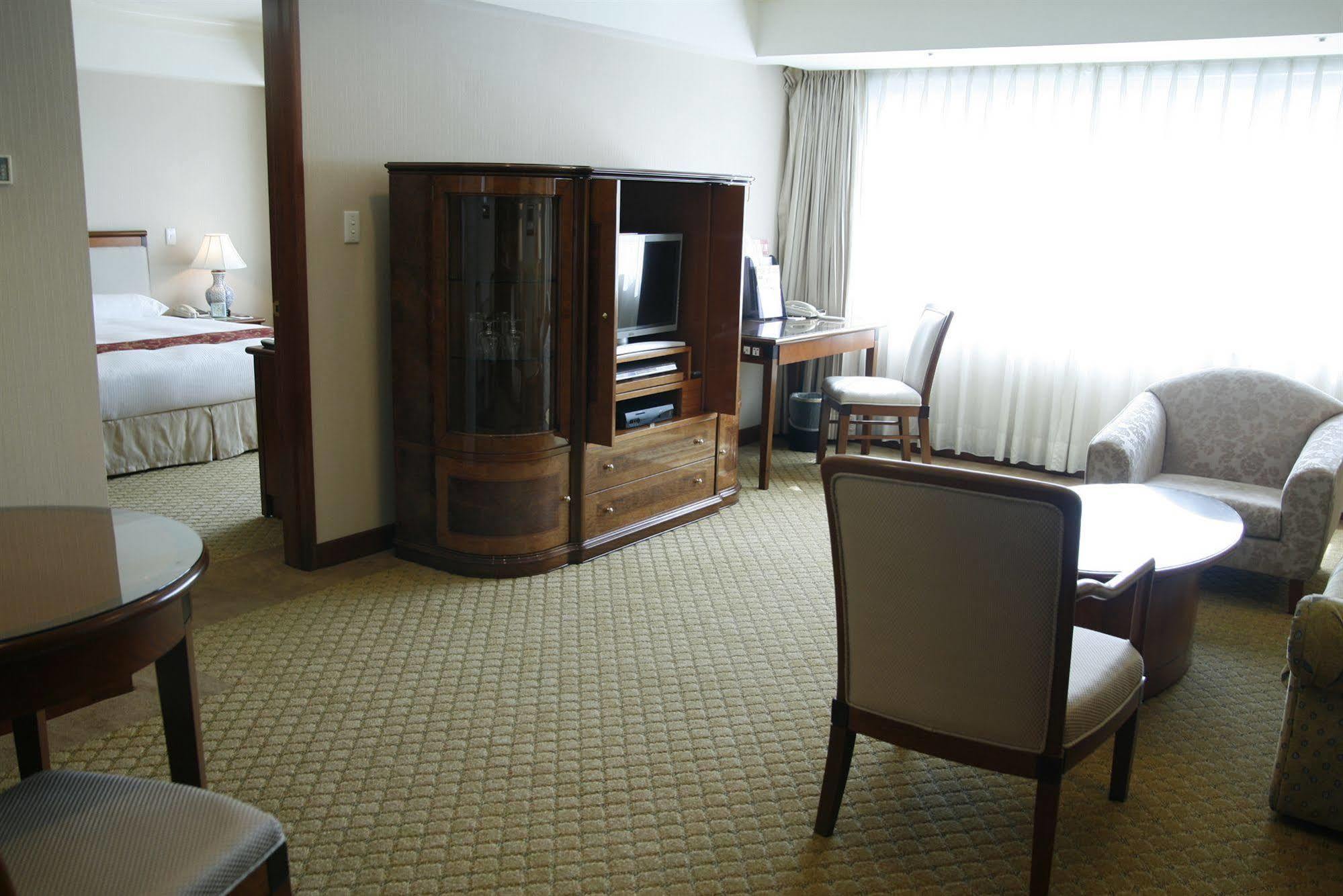Evergreen Laurel Hotel - Тайчжун Экстерьер фото The photo shows an interior of a hotel room suite. The space includes a living area with several pieces of furniture. There is a coffee table and chairs, creating a comfortable seating area. A wooden cabinet with a TV inside is situated against one w
