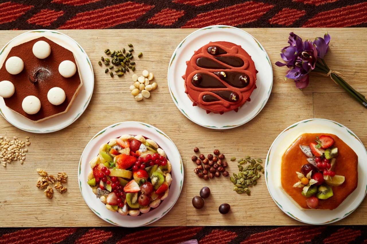 Evergreen Laurel Hotel - Тайчжун Экстерьер фото The photo displays a variety of desserts arranged on small plates. There are three main cakes or tarts:

1. **Top Left Plate**: A round chocolate cake with a smooth surface and white decorations on top.
2. **Top Middle Plate**: Another cake, possibly