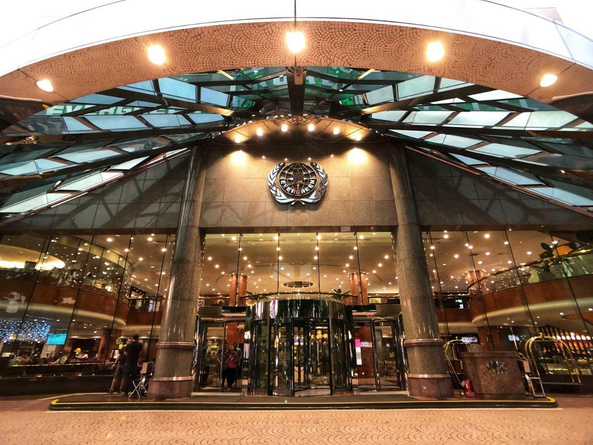 Evergreen Laurel Hotel - Тайчжун Экстерьер фото The image shows the entrance of a modern building, likely a hotel or a luxury establishment. The entrance features a large revolving door surrounded by glass panels. Above the entrance, there is a prominent logo or emblem. The overall architectural d