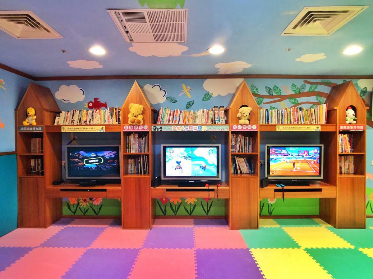 Evergreen Laurel Hotel - Тайчжун Экстерьер фото The photo shows a colorful and playful room designed for children. In the center, there are three wooden gaming stations, each equipped with a television screen and surrounded by shelves filled with books. The walls are decorated with cheerful images