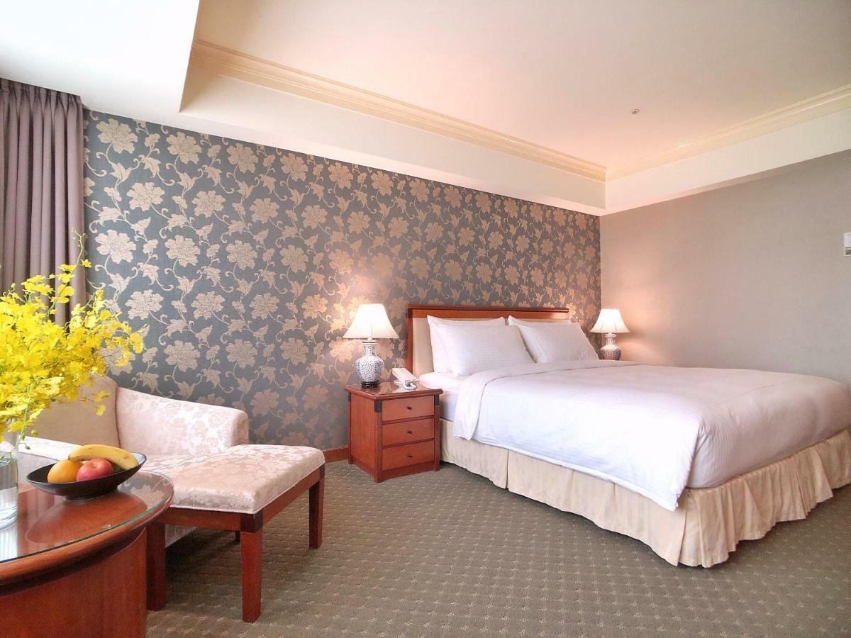 Evergreen Laurel Hotel - Тайчжун Экстерьер фото The photo shows a well-decorated hotel room. It features a large bed with white bedding, situated against a patterned wall with floral designs. On either side of the bed are bedside tables with lamps. There is a small seating area that includes a cha