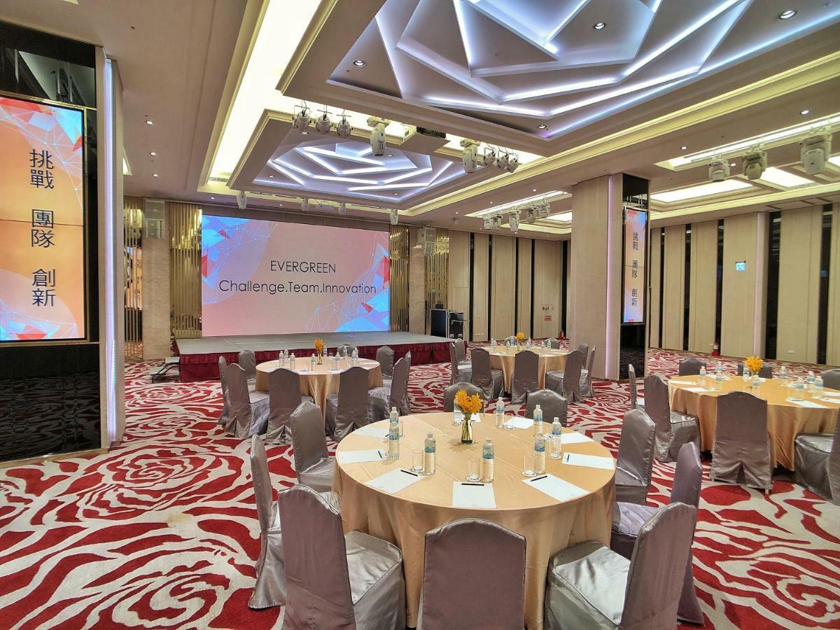Evergreen Laurel Hotel - Тайчжун Экстерьер фото The photo shows a conference or event space set up for a gathering. The room features several round tables with light-colored tablecloths and chairs, each with decoration, possibly for dining or discussion. A large screen displays the text "EVERGREEN