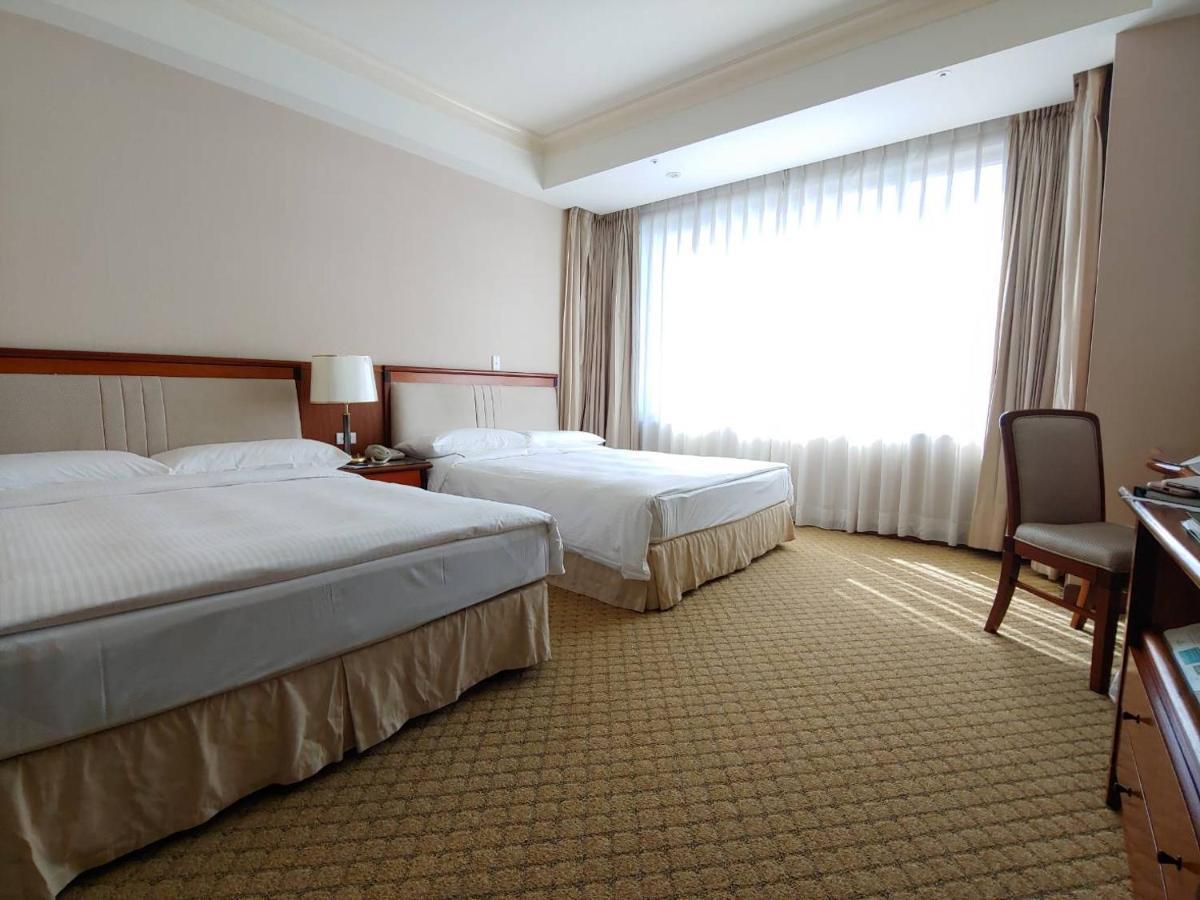 Evergreen Laurel Hotel - Тайчжун Экстерьер фото The photo shows a neatly arranged hotel room featuring two beds: one double bed and one single bed. The room has beige walls and a warm color palette. Large windows with sheer curtains allow natural light to flood in, creating a bright and airy atmos